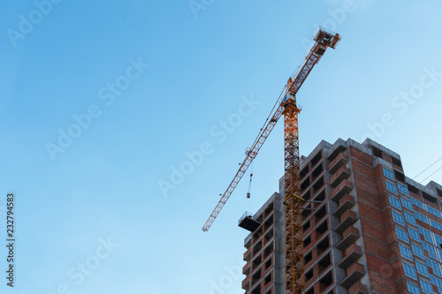 orange tower building crane near the new house under construction on the blue sky background. photo