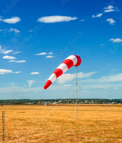 red and white windsock wind sock on blue sky on the aerodrome, yellow field and clouds background in autumn