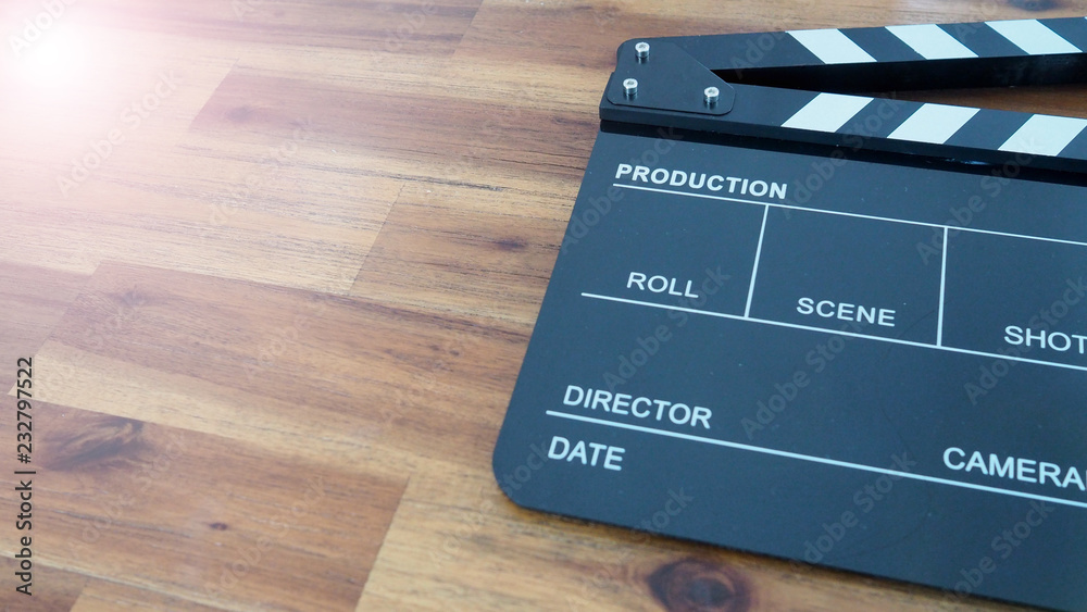 Clapper board or movie slate use in video production or movie and cinema industry. It's black color on wood background with flare light.