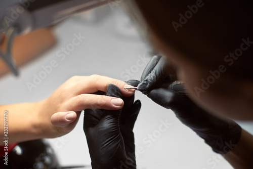 Close-up of professional master manicurist hands working on client woman fingernails with electric drill file on light gray background. Finger nail treatment  fashion  manicure making in beauty salon.