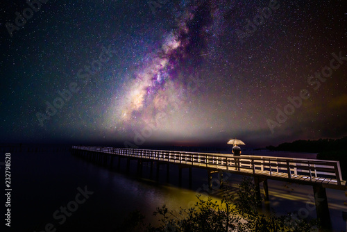 milky way on the sky and some one use umbrella with lighting on the bridge