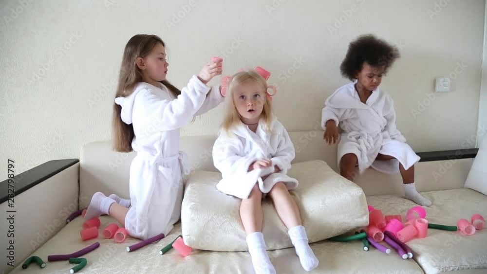Little girls play with hair curlers and hairpins. Girls girlfriends in white coats braid curlers and hair clips each drg in her hair. Little girls play with hair curlers and hairpins. Girls girlfriends in white coats braid curlers and hair clips each drg in her hair.