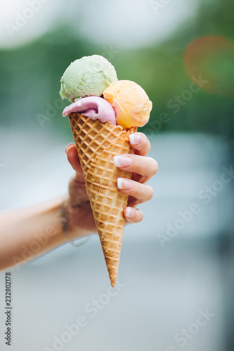 Tender woman's hand keeping delicious colorful ice cream. Lookinf very tasty, sweet, mouthwatering, perfect for summer heat while sunny day. Pretty nails with professional french manicure. Soft focus.