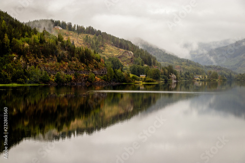 Beautiful reflection in the Tyrifjorden (Lake Tyri) after a rainy day in Norway. Dramatic sky, fog, trees and mountains are perfectly mirrored in the lake. © Dennis Wegewijs