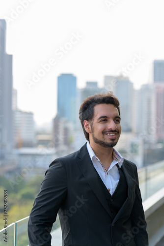 Thoughtful young happy Indian businessman smiling at rooftop in 