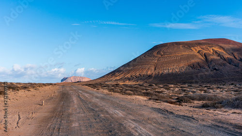 Dirt road going through a spectacular volcanic landscape on a blue sky summer day. Hiking path in La Graciosa Island, Canary, Spain.