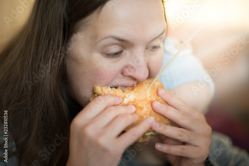 Closeup portrait. Beautiful young woman having fun eating big burger.