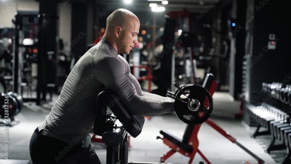 Muscular man in sportswear training in the gym with a barbell doing biceps exercise Muscular man in sportswear training in the gym with a barbell doing biceps exercise