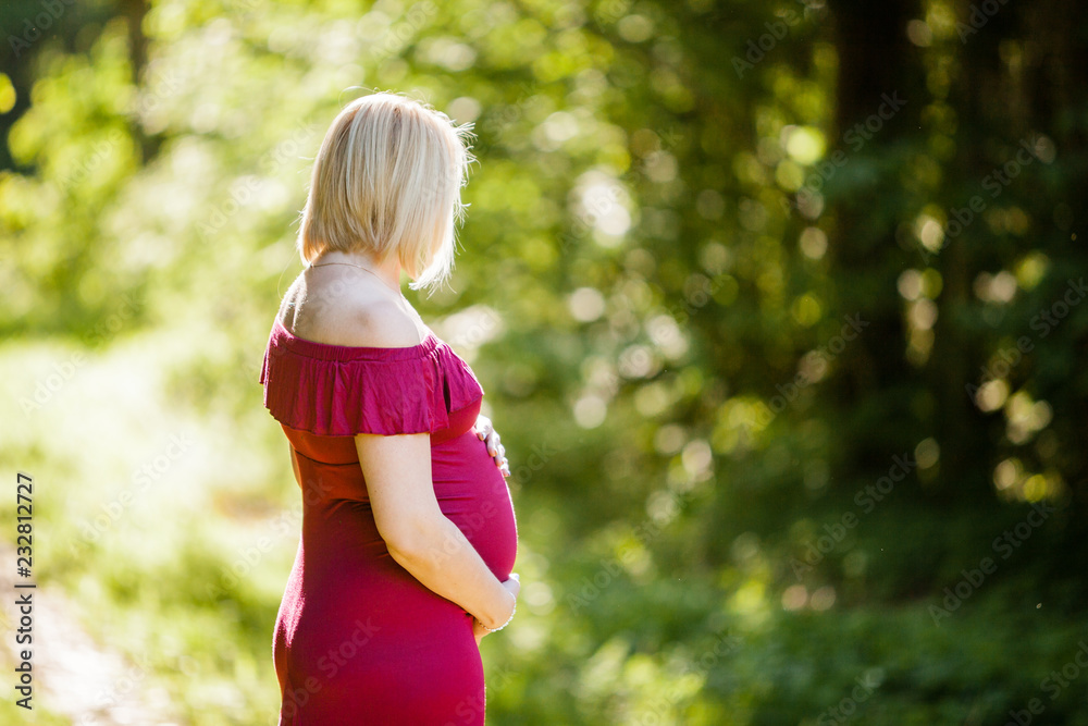 Fototapeta premium Portrait of beautiful pregnant woman in stylish long purple maternity dress looking dreamy in the middle of forest