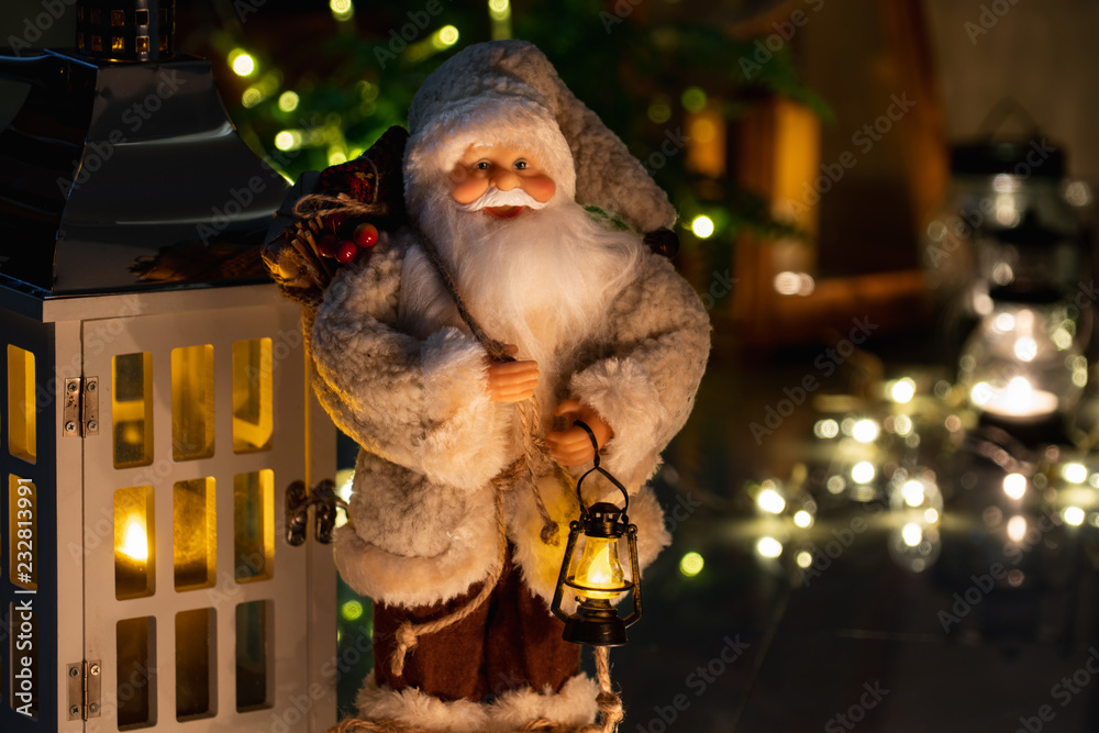 Christmas decoration with a toy Santa Claus, wooden lantern, candles and garlands.