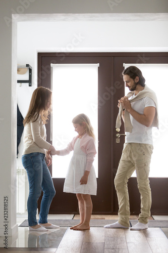 Young parents and preschool daughter standing in corridor hall of their new home opposite front door. Loving mother holding little girl hand Gathering for a walk in good day and family weekend concept