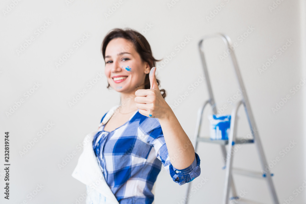 Repair, renovation and people concept - young woman painting the wall and looks like very happy, she showing thumb up Repair, renovation and people concept - young woman painting the wall and looks like very happy, she showing thumb up