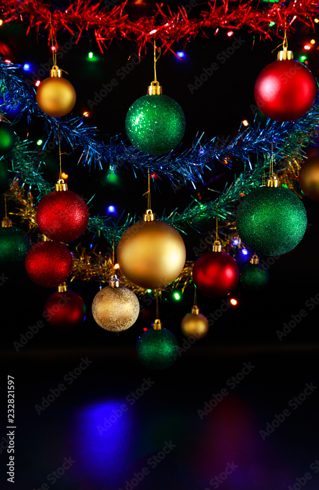 Close up of hanging Christmas decorations against a black background.