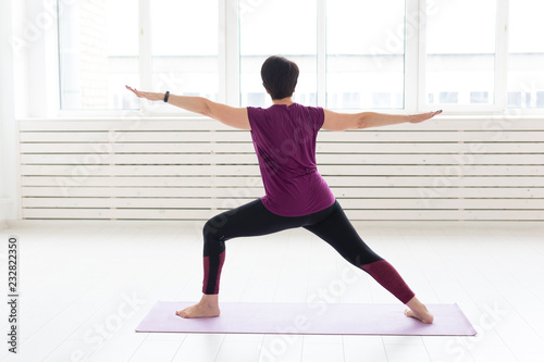 People, sport and healthcare concept - Middle-aged woman practicing yoga, standing in Warrior two exercise