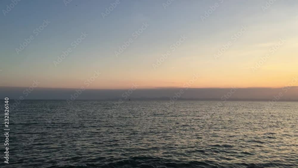 Sunset at sea with narrow line of the city far away. Seagulls are flying Sunset at sea with narrow line of the city far away. Seagulls are flying