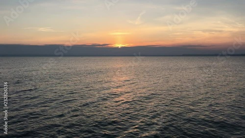 Sunset at sea with narrow line of the city far away. Seagulls are flying 