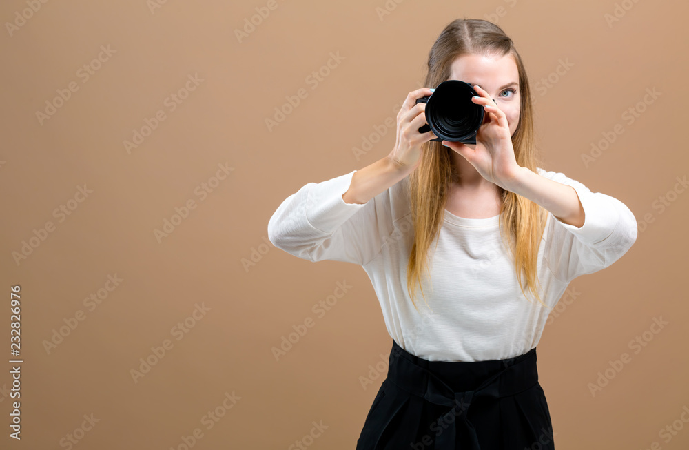 Young woman with a professional digital SLR camera on a brown background Young woman with a professional digital SLR camera on a brown background