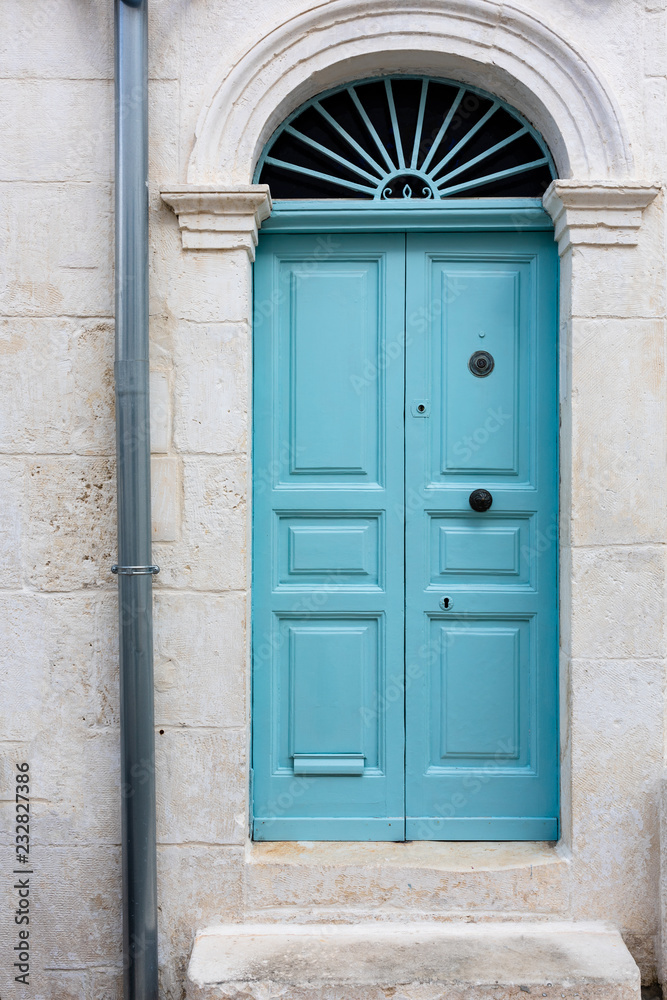 An aquamarine colored door on a white house in the Puglia region of Italy