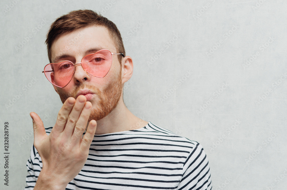 Young man in pink glasses. Valentine's day holiday. Light background. Kiss Young man in pink glasses. Valentine's day holiday. Light background. Kiss