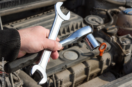 wrench in the hands of a man on the background of the open hood of the car. auto repair shop, repair of vehicles.