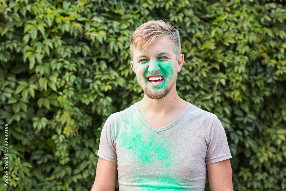 Holiday, holi and people concept - Smiling man posing with green powder on his shirt and face. Holiday, holi and people concept - Smiling man posing with green powder on his shirt and face.
