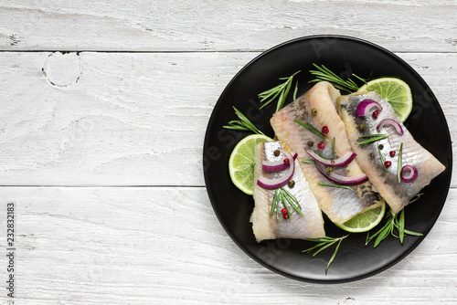 herring fillet with pepper, rosemary, onion and lime on black plate on white background. top view with copy space