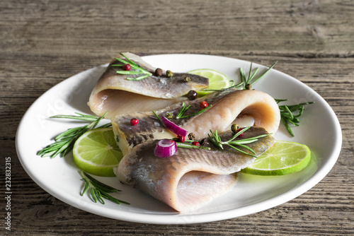 fillet of herring with pepper, rosemary, onion and lime in a plate on rustic wooden background. close up