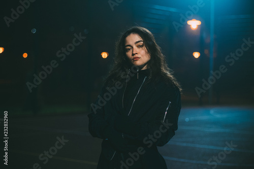 Young caucasian girl on basketball playground in night time and low exposure