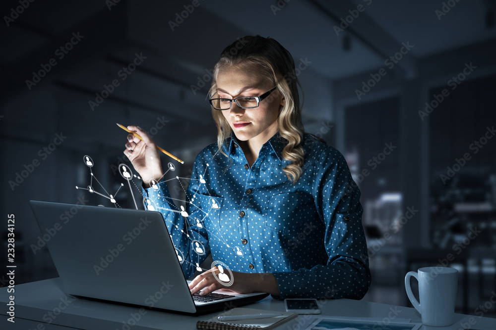 Attractive blonde wearing glasses in dark office using laptop. M Attractive blonde wearing glasses in dark office using laptop. M