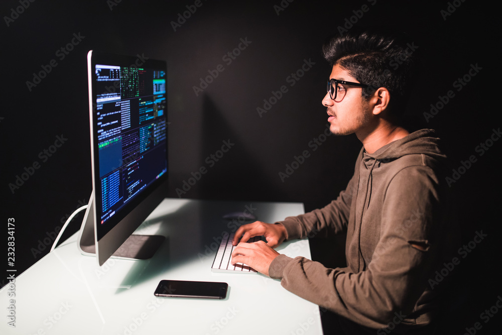 Program development concept. Young indian man working with computer on dark background