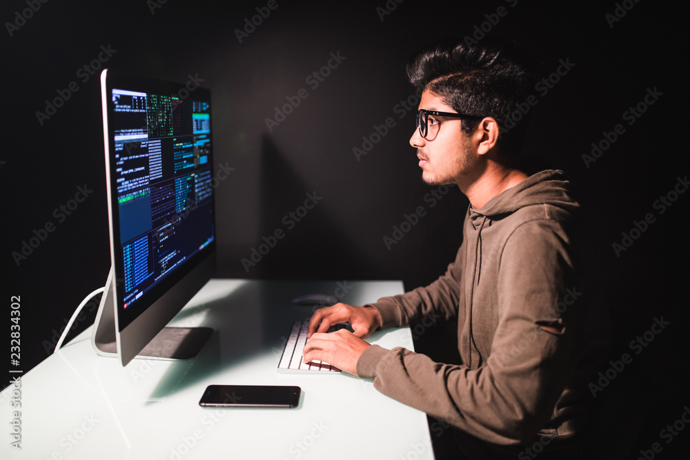 Indian man programmer working on desktop computer at white desk in office. Indian man programmer working on desktop computer at white desk in office.