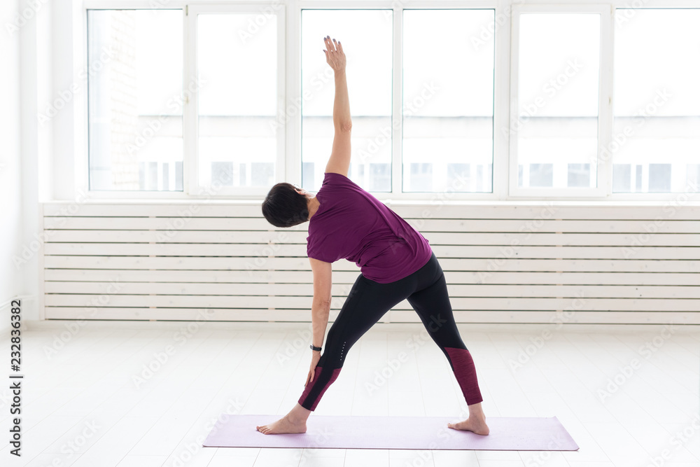 Yoga, harmony, people concept - a middle-aged woman is practicing the yoga and looking in the window Yoga, harmony, people concept - a middle-aged woman is practicing the yoga and looking in the window