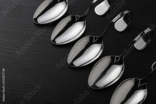 many steel spoons on a black surface, lined up, concept, top view, close-up shot