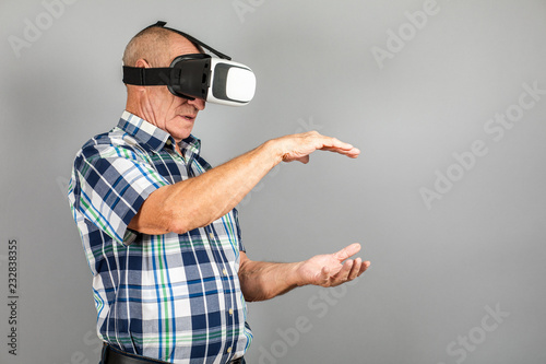 Grandfather looks into VR glasses, hand gestures, on a gray background.