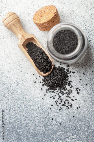 Black cumin seeds on a wooden spoon and in a glass jar on gray background