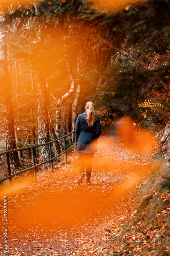 A blonde young girl in the mountain forest with colorful fall color tones and moody environment scene in dark winter. Okertal, Oker gorge, Oker National Park Harz, Harz Mountains, Germany