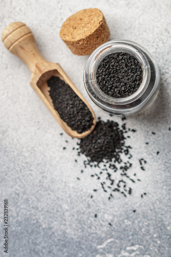 Black cumin seeds on a wooden spoon and in a glass jar on gray background