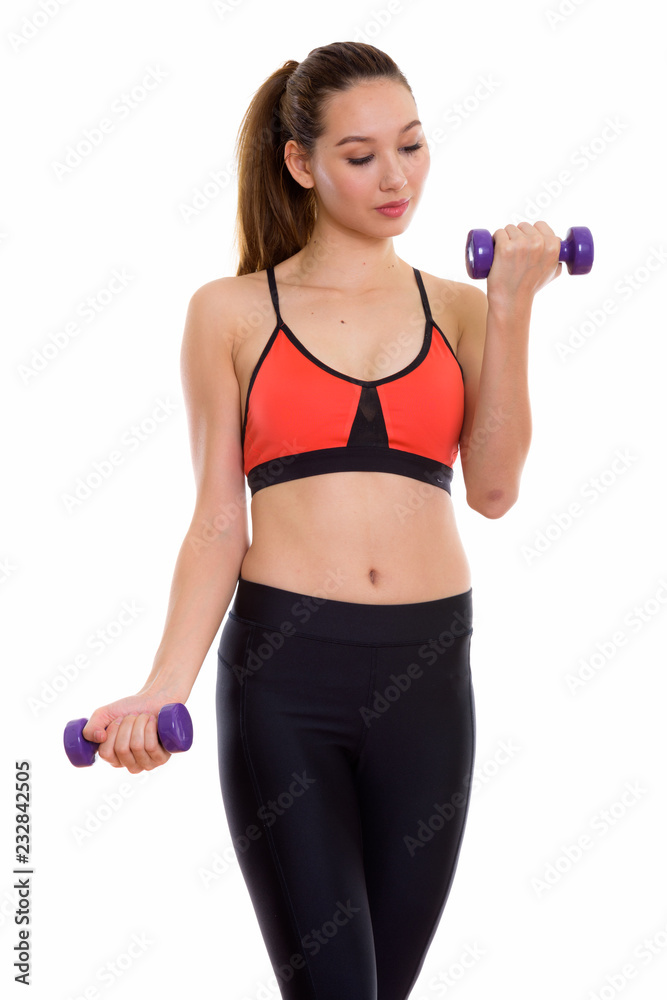 Studio shot of young beautiful Asian woman looking at dumbbells Studio shot of young beautiful Asian woman looking at dumbbells