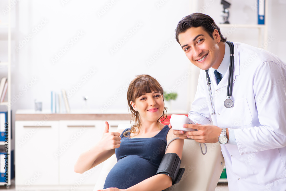 Fototapeta premium Young doctor checking pregnant woman's blood pressure