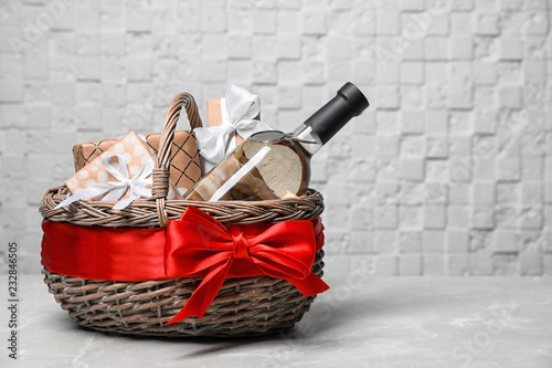 Gift basket with bottle of wine on light background. Space for text