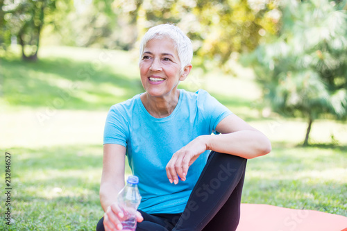 Senior sportive woman sitting on mat outside and resting