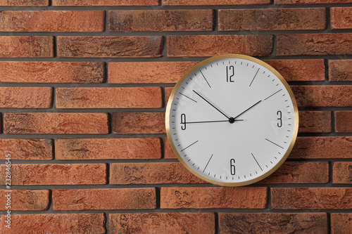 Stylish analog clock hanging on brick wall. Space for text