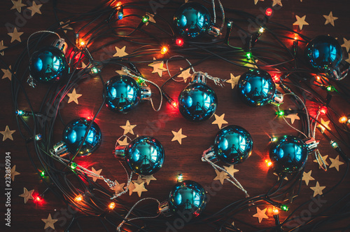 Beautiful blue christmas balls, golden star confetti and a glowing garland on the wooden table top view
