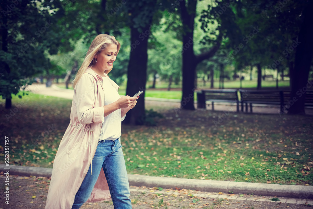 Pretty blonde woman walk in the park and look at smartphone Pretty blonde woman walk in the park and look at smartphone