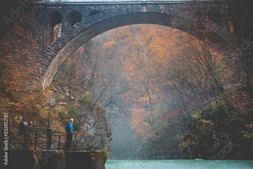 Man standing under old bridge in autumn landscape. Vintgar, Slovenia