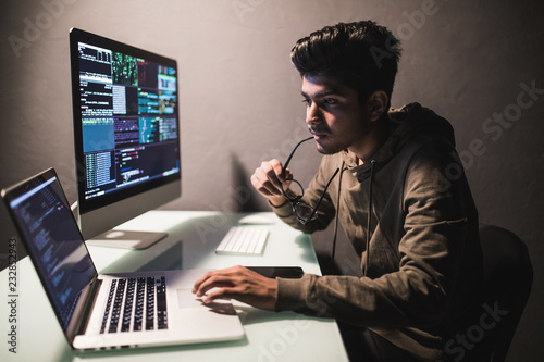 Program development concept. Young indian man working with computer in dark office photo