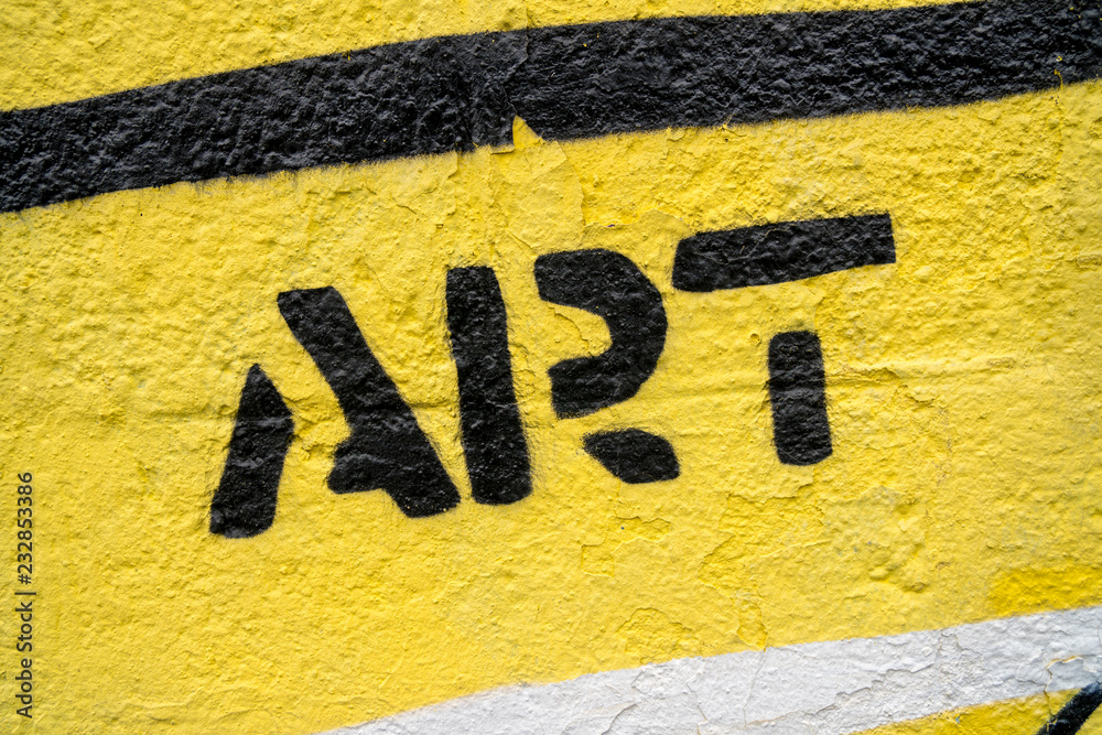 Fototapeta premium Fragment rysunku graffiti. Słowo „art” w kolorze czarnym na żółtej starej ścianie ozdobionej farbą w stylu street art.