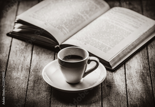 Little a cup of coffee and open book on a wooden table. Image in white and black color style