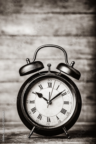 classic alarm clock with bell on wooden table. Photo in black and white image style.