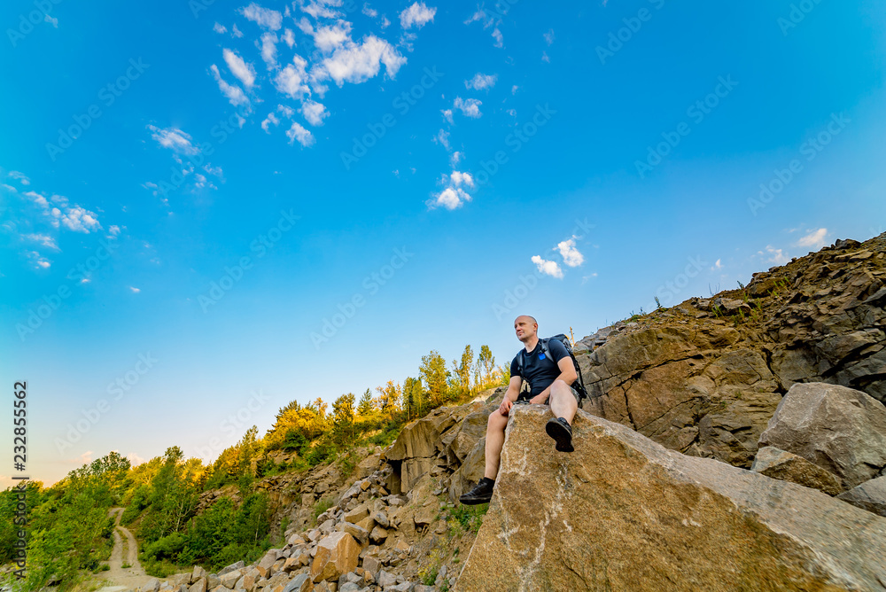 Male hiker with backpack relaxing at the edge of a huge rock. Tourist enjoys a beautiful view from the rock.